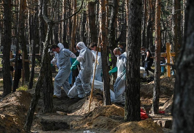 Forensic technicians carry a bodybag at the site of a mass grave in a forest on the outskirts of Izyum, eastern Ukraine on 18 September, 2022