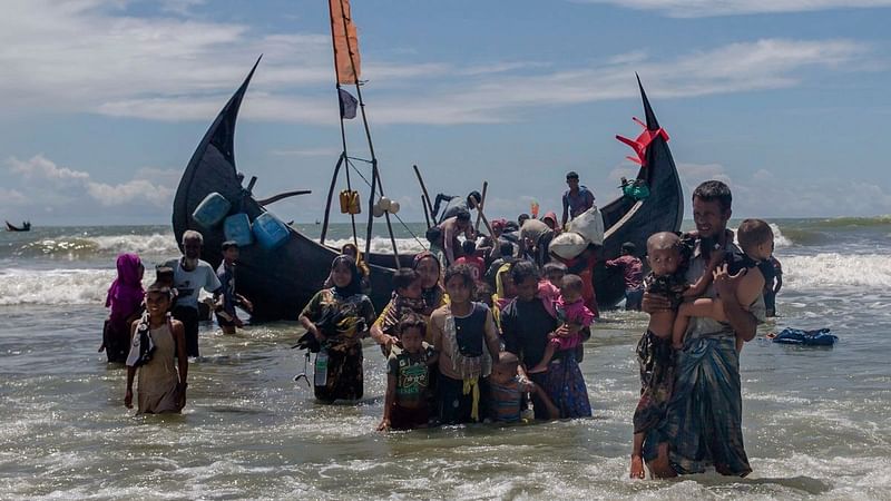 In this 14 September 2017 file photo, a Rohingya man carries two children to shore in Shah Porir Dwip, Bangladesh, after they arrived on a boat from Myanmar. The UN refugee agency says nearly 69 million people who have fled war, violence and persecution were forcibly displaced last year, a new record for the fifth straight year. The UN High Commissioner for Refugees said Tuesday, 19 June 2018 that continued crises in places like South Sudan and Congo, as well as the exodus of Muslim Rohingya from Myanmar starting last year, raised the overall figure of forced displacements in 2017 to 68.5 million.