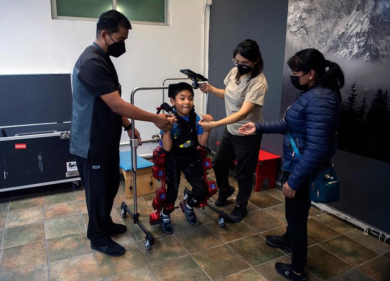 David Zabala, an 8-year-old boy with cerebral palsy, is assisted by physical therapists and his mother, Guadalupe Cardozo Ruiz (R), during a rehabilitation session with the robotic exoskeleton Atlas 2030 at the Association for People with Cerebral Palsy (APAC) in Mexico City on 18 October, 2022.