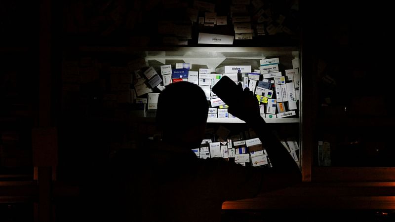 A salesman of a pharmaceutical shop uses his cellphone torch to find medicine to serve customers during a countrywide blackout in Dhaka, Bangladesh, on 4 October, 2022