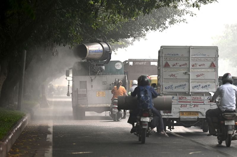 Commuters ride past an anti-smog gun spraying water to curb air pollution amid heavy smog conditions in New Delhi on 4 November, 2022.