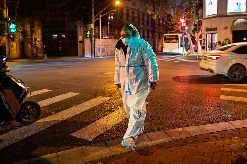 A worker wearing a protective equipment (PPE) walks on a street in the Xuhui district in Shanghai on 19 December, 2022