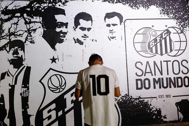 A person stands in front of an image depicting Brazilian football legend Pele as people gather to mourn his death, in Santos, Brazil on 29 December, 2022.