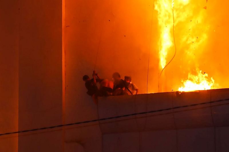 People gather on a ledge as a fire burns around them at the Grand Diamond City hotel-casino in Poipet on 28 December, 2022