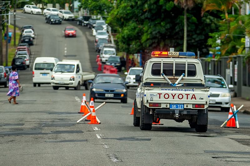 A woman crosses a street near a police vehicle parked at a security check post on the streets of Suva on December 23, 2022, a day after the government announced a post-election military deployment to maintain "law and order"