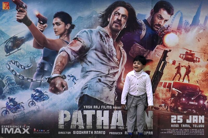 A boy plays in front of a poster of the Bollywood movie 'Pathaan' outside a cinema hall in Prayagraj on 25 January, 2023. Bollywood megastar Shah Rukh Khan returned to the silver screen on January 25 for the first time in four years with an action-packed rollercoaster film that has sparked ire from Hindu right-wingers.