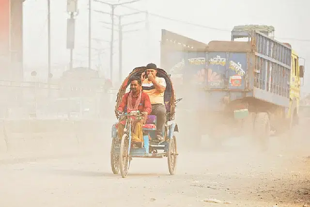 A rickshaw passenger covers his mouth and nose as dust fills the air above the dilapidated road. Photo taken recently at Aminbazar