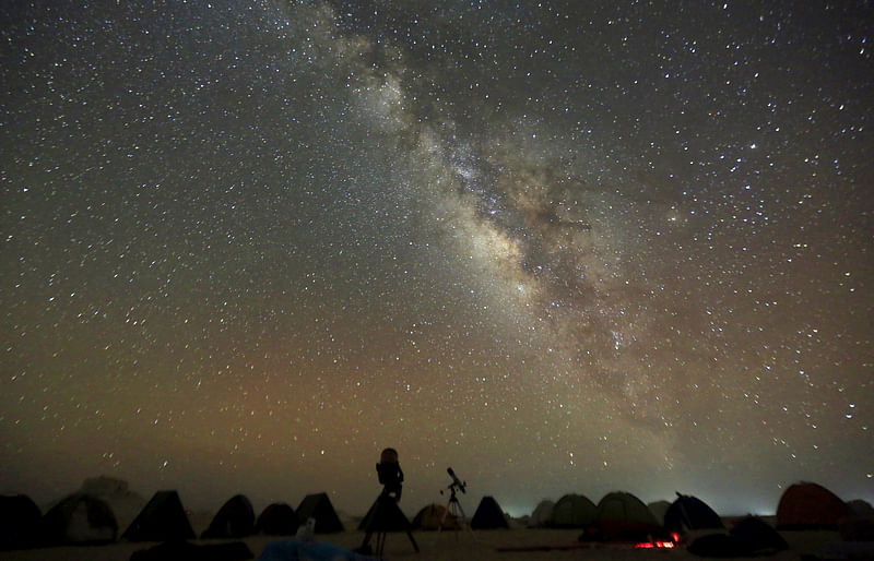 The Milky Way is seen in the night sky around telescopes and camps of people over rocks in the White Desert north of the Farafra Oasis southwest of Cairo 16 May, 2015.