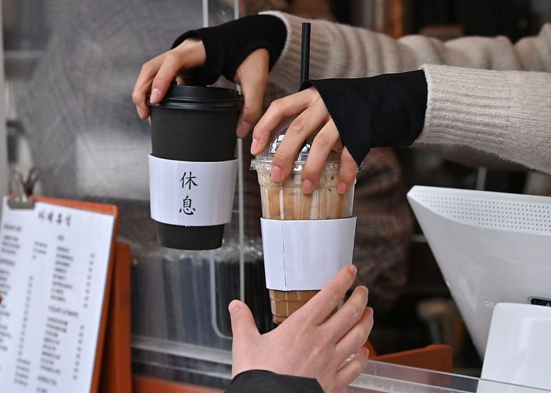 This picture taken on 26 January, 2023 shows an employee passing out hot and cold coffee drinks to a customer at a cafe in Seoul. K-pop stars BTS drink it. It appears in K-dramas. Fans are so dedicated to consuming it year-round they've coined a new South Korean proverb: "even if I freeze to death, iced Americano!"