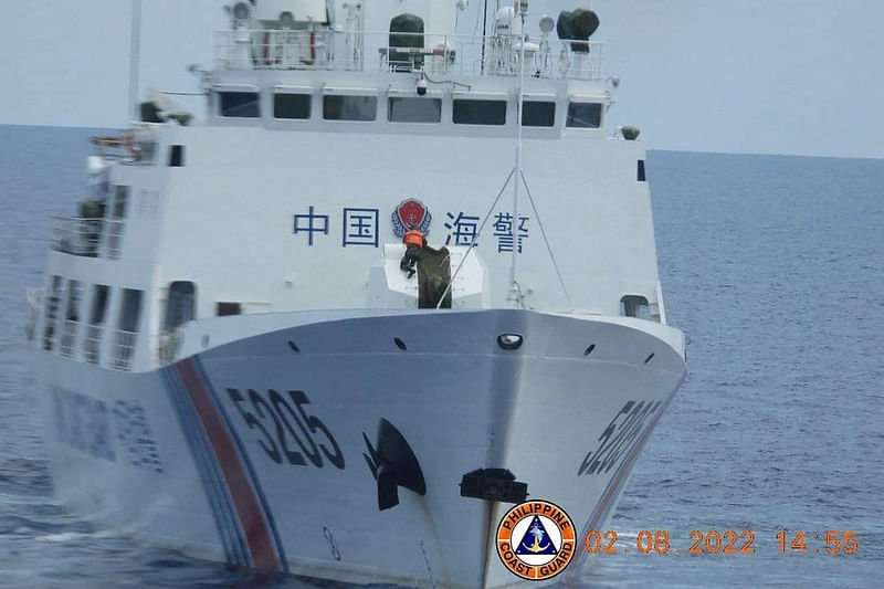 This handout photo taken on August 8, 2022 and released by the Philippine Coast Guard on 13 February, 2023 shows a sailor (C, in orange vest) on board a Chinese Coast Guard vessel removing a cover of its '70 mm naval armament'