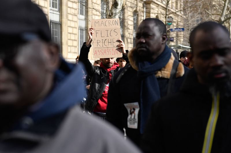 A demonstrator holds a placard reading "Macron + cops +rich, murderers" during a march to denounce "state violence and systemic racism", in Paris on 18 March, 2023