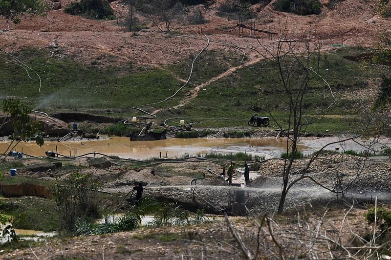 Informal miners look for gold in the Nechi river in Caucasia municipality, Antioquia department, Colombia on 23 March 2023. The giant skeletons of burnt and dismantled gold dredgers litter the rivers of northwest Colombia, where the government is waging a full-out war on illegal mining. Nicknamed "dragons" by locals, the massive machines used to suck gold from river beds are blamed for destroying the environment and financing organized crime. But their dismantling in a massive army operation has been met with hostility by communities who depend on mining for their daily survival.