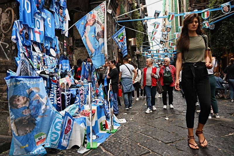 A woman passes by a stall selling Napoli gadgets in Via Tribunali, in district of Forcella in central Naples on 29 April 2023, on the eve of the Italian Serie A football match between Napoli and Salernitana