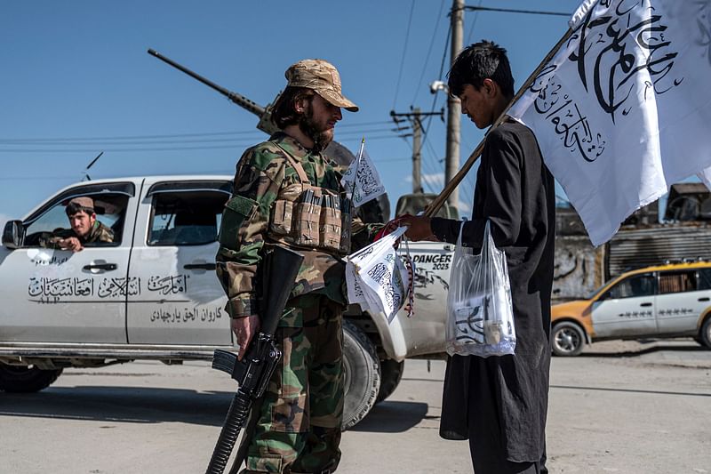 A Taliban security personnel talks with a flag vendor outside the Eid Gah mosque in Kabul on April 20, 2023