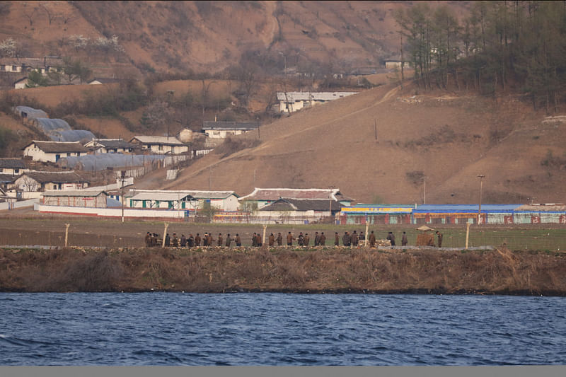 Men at a field in North Korea's Sinuiju are seen from Dandong, Liaoning province, China 20 April, 2021