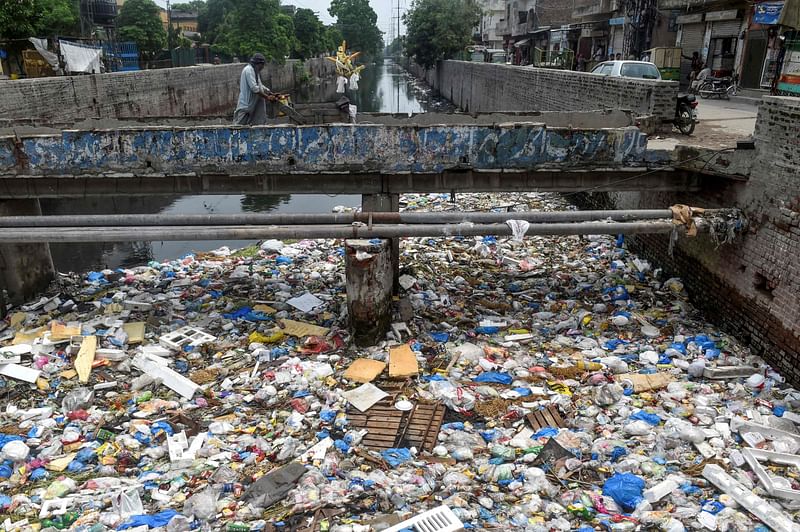 In this picture taken on 31 July 2019, a vendor pushes his corn cart over a stream full of plastic bags and garbage in Lahore. Negotiations on a global treaty to combat plastic pollution will resume on 29 May 2023, with nations under pressure to stem the tide of trash amid calls from campaigners to limit industry influence on the talks.