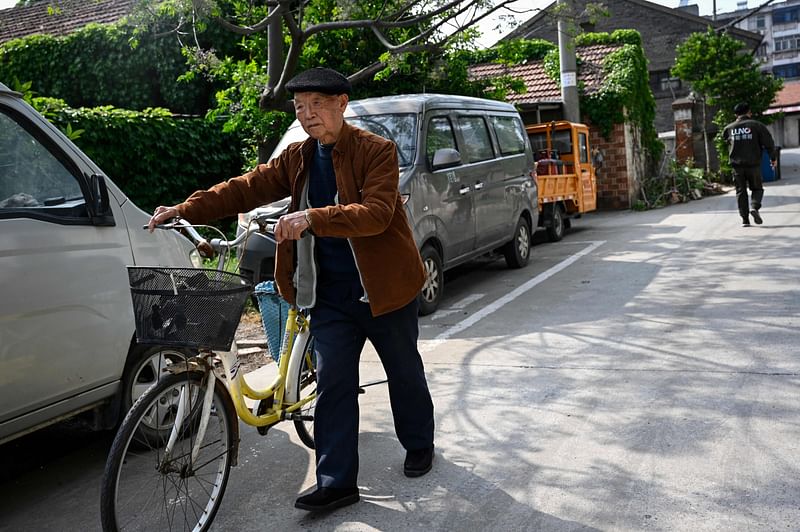 This photo taken on April 27, 2023 shows an elderly man pushing his bicycle through a residential area in Rudong, in eastern China’s Jiangsu province. Rudong once played a pioneering role in the rollout of Beijing's one-child policy