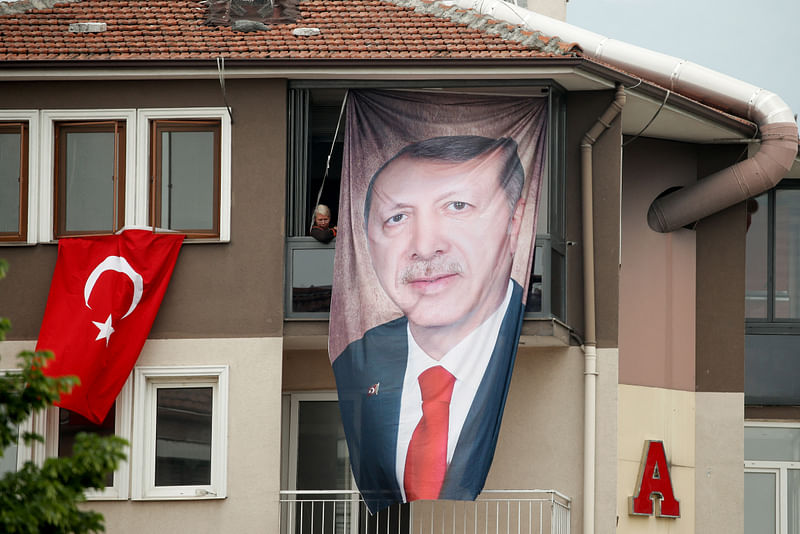 A woman looks out of a building with a poster of Turkish President Tayyip Erdogan as supporters of Kemal Kilicdaroglu, presidential candidate of Turkey's main opposition alliance, gather during a rally ahead of the 14 May presidential and parliamentary elections, in Bursa, Turkey on 11 May, 2023.