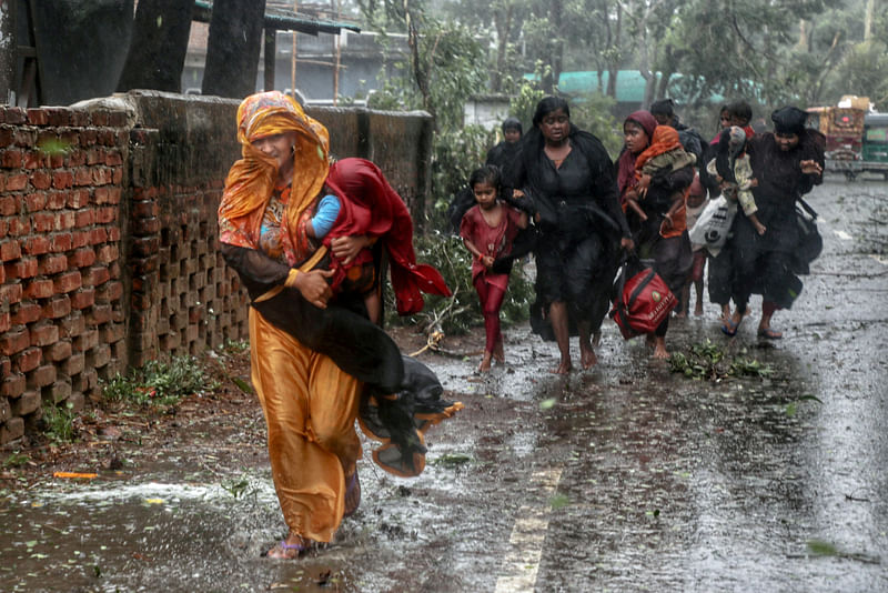 People move from their homes to take shelter in the nearest cyclone shelter at Shah Porir Dwip during the landfall of cyclone Mocha in Teknaf, Bangladesh, 14 May 2023.