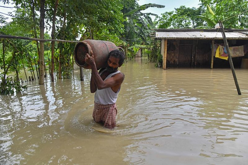 A man carries belongings from his partially submerged house in the flood affected Dhamdhama village of Nalbari district, in India's Assam state on 22 June, 2023