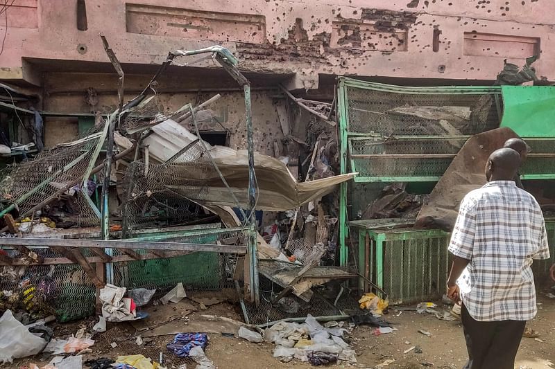 People walk past a medical centre building riddled with bullet holes at the Souk Sitta (Market Six) in the south of Khartoum on 1 June, 2023