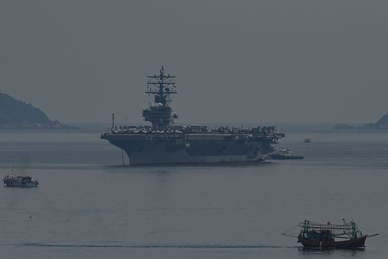 A Vietnamese fishing boat (R) sails past the USS Ronald Reagan (C), a US Navy Nimitz-class nuclear-powered aircraft carrier, in Danang on June 25, 2023