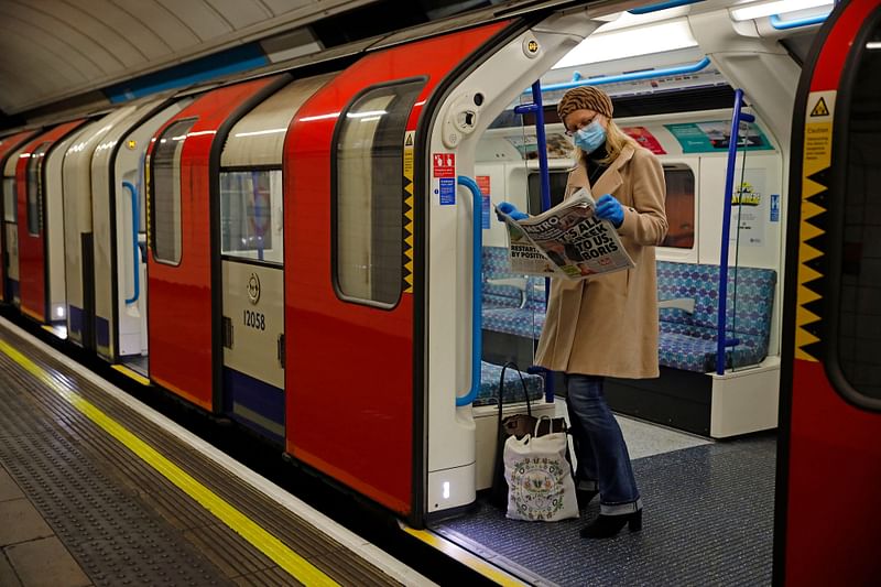 A woman wearing PPE (personal protective equipment), including a face mask as a precautionary measure against COVID-19, reads a newspaper as she stands aboard a London Underground Tube train, in the morning rush hour on May 11, 2020, as life in Britain continues during the nationwide lockdown due to the novel coronavirus pandemic. An enquiry probing the UK government's handling of the coronavirus pandemic kicks off Tuesday with the investigation mired in controversy even before the first witness is called