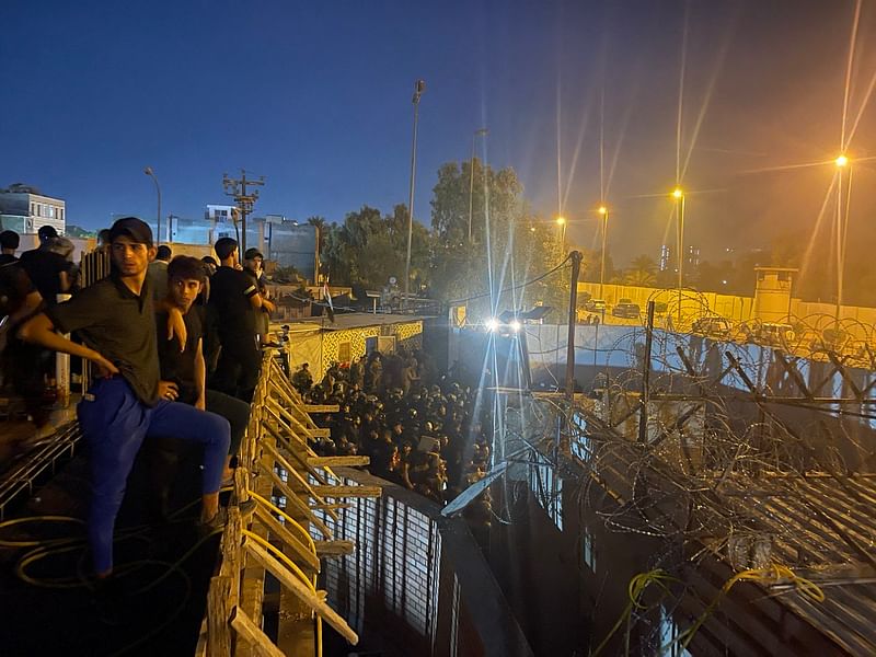 Protesters stand on top of a building overlooking a street full of Iraqi riot policemen leading to the Swedish embassy in Baghdad on July 20, 2023.