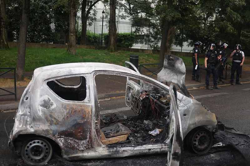 French police officers in riot gear stand next to a burnt car at the Pablo Picasso neighbourhood in Nanterre on 1 July, 2023