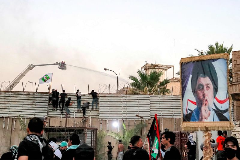 Supporters of Iraqi Shiite cleric Moqtada al-Sadr during a protest climb the fence outside the Swedish embassy in Baghdad on 20 July, 2023 as firefighters try to put out a fire there. Protesters set fire to Sweden's embassy in the Iraqi capital early on 20 July ahead of a planned burning of a Quran in Sweden