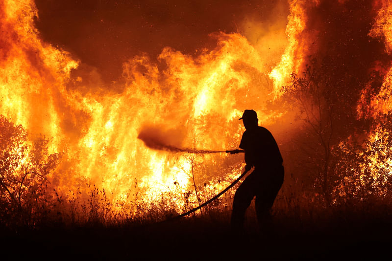 A firefighter tries to extinguish a wildfire burning at the industrial zone of the city of Volos, in central Greece, July 26, 2023