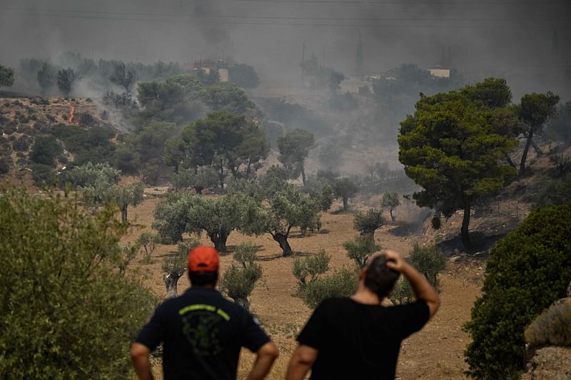 A firefighter (L) and a local resident react as they look at a wildfire in a forest near Nea Peramos, west of Athens on 19 July, 2023