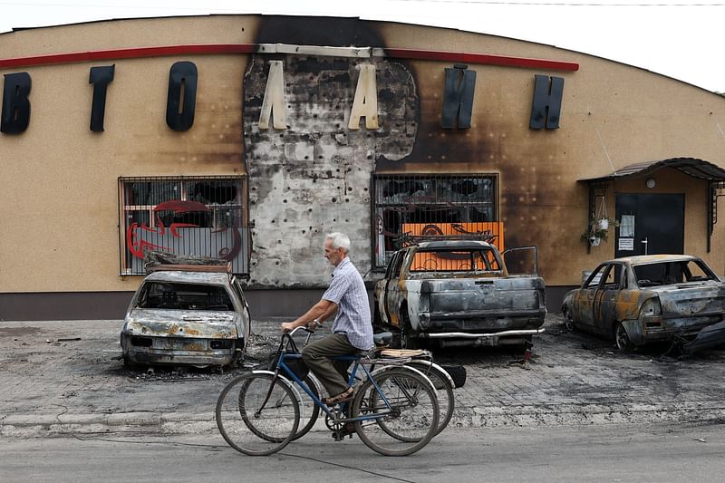 An elderly man riding a bicycle pushes the bike of his wife killed by a cluster bomb in Lyman, Donetsk region, on July 8, 2023