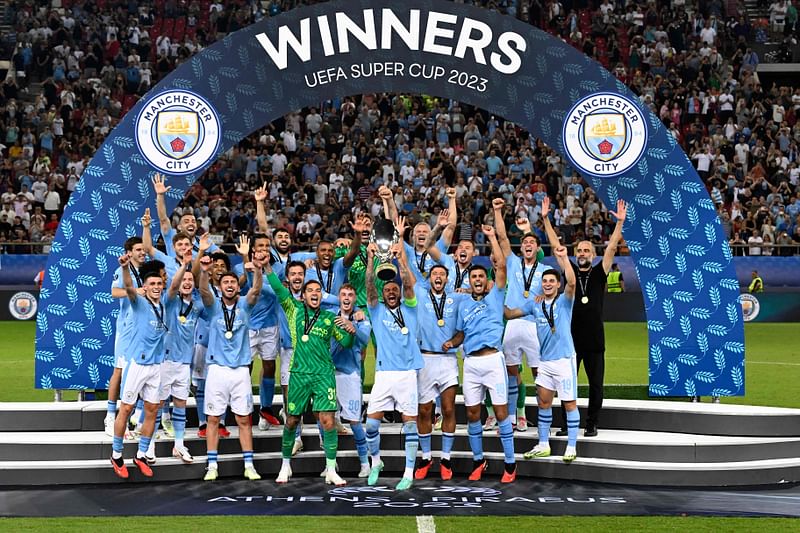 Manchester City's players celebrate on the podium after winning the 2023 UEFA Super Cup football match between Manchester City and Sevilla at the Georgios Karaiskakis Stadium in Piraeus on 16 August, 2023