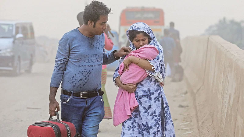 A woman covers her baby with a fabric to protect the baby as the road is engulfed with dusts in Postagola area, Dhaka.