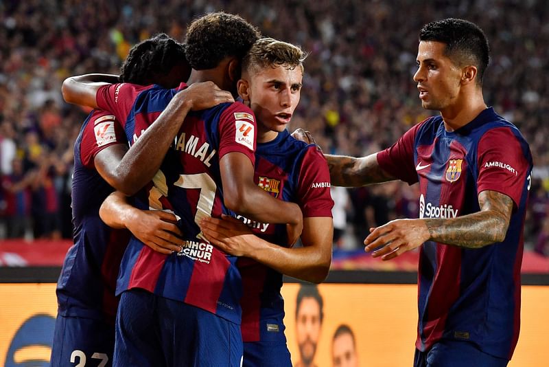 Barcelona's Spanish forward #27 Lamine Yamal, Barcelona's Spanish midfielder #32 Fermin Lopez (C) and Barcelona's Portuguese defender #02 Joao Cancelo (R) celebrate Sevilla's Spanish defender #04 Sergio Ramos' own goal during the Spanish Liga football match between FC Barcelona and Sevilla FC at the Estadi Olimpic Lluis Companys in Barcelona on 29 September, 2023.