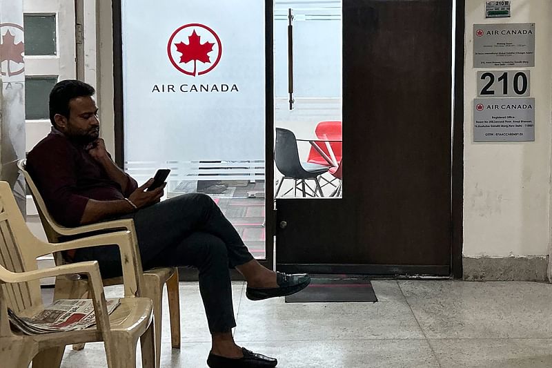 A man checks his mobile as he sits outside an Air Canada regional office in New Delhi on 20 September, 2023.