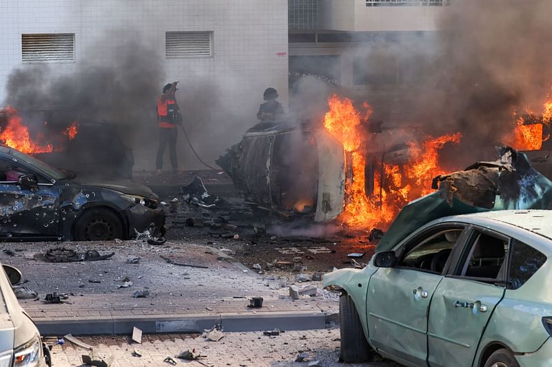 People try to extinguish fire on cars following a rocket attack from the Gaza Strip in Ashkelon, southern Israel, on October 7, 2023. Palestinian militant group Hamas has launched a "war" against Israel, Defence Minister Yoav Gallant said, after barrages of rockets were fired from the Gaza Strip into Israeli territory on October 7