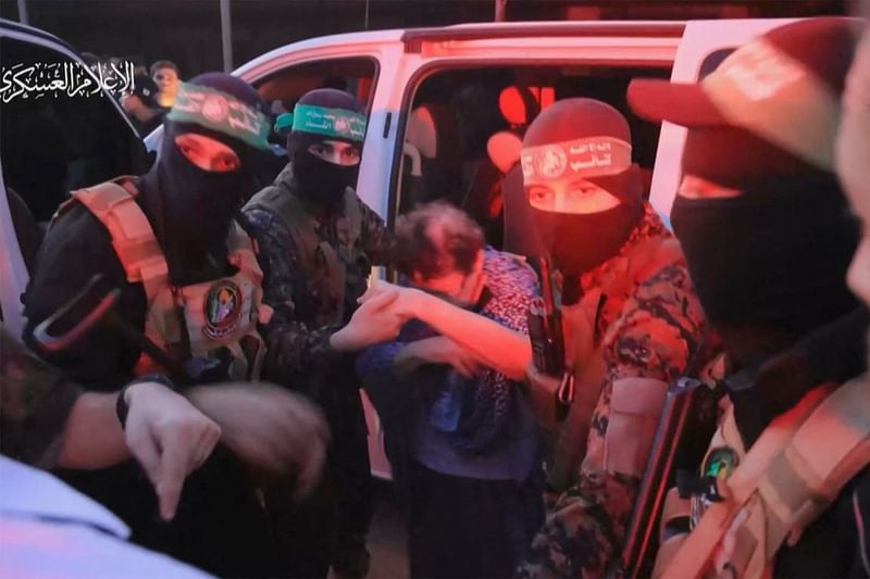 An image grab from a handout video released by the Hamas Media Office shows a member of its Al-Qassam Brigades helping a hostage out of a car before handing them over to officials from the International Committee of the Red Cross in Gaza on 24 November, 2023