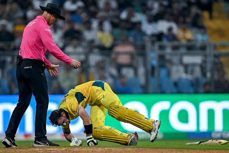 Australia's Glenn Maxwell (R) falls on the ground after a muscle cramp during the 2023 ICC Men's Cricket World Cup one-day international (ODI) match between Australia and Afghanistan at the Wankhede Stadium in Mumbai on 7 November, 2023