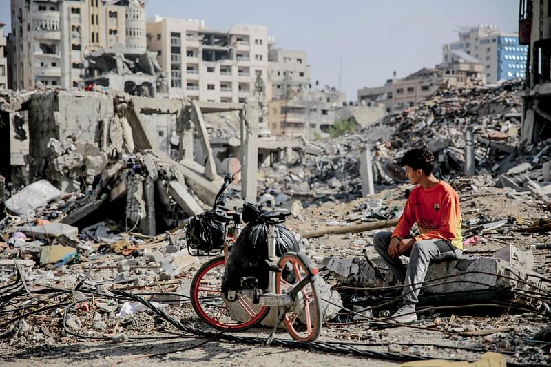 A Palestinian youth sits next to his bicycle amid the rubble of destroyed buildings in Gaza City on the northern Gaza strip following weeks of Israeli bombardment, as a four-day ceasefire took effect on 24 November 2023