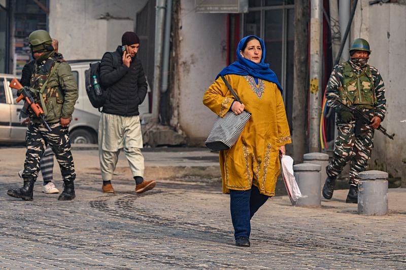 People walk along a street as Indian paramilitary personnel patrol in Srinagar on 11 December 2023, ahead of Supreme Court's verdict on Article 370.