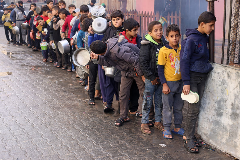 Palestinian children carry pots as they queue to receive food cooked by a charity kitchen, amid shortages in food supplies, as the conflict between Israel and Hamas continues, in Rafah in the southern Gaza Strip December 14, 2023