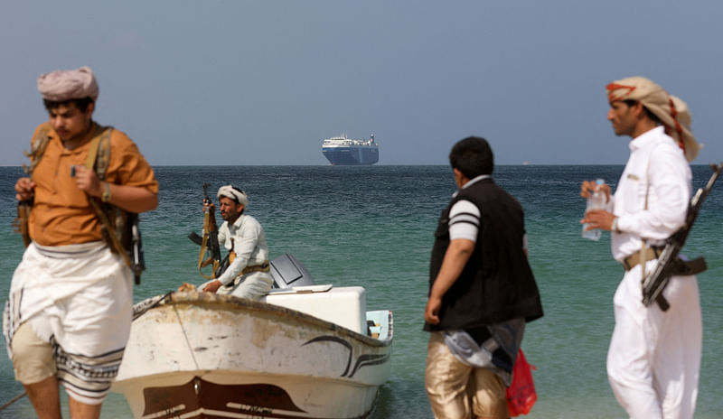 Armed men stand on the beach as the Galaxy Leader commercial ship, seized by Yemen’s Houthis last month, is anchored off the coast of al-Salif, Yemen, on 5 December, 2023