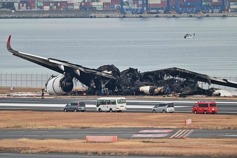 Officials look at the burnt wreckage of a Japan Airlines (JAL) passenger plane on the tarmac at Tokyo International Airport at Haneda in Tokyo on January 3, 2024, the morning after the JAL airliner hit a smaller coast guard plane on the ground