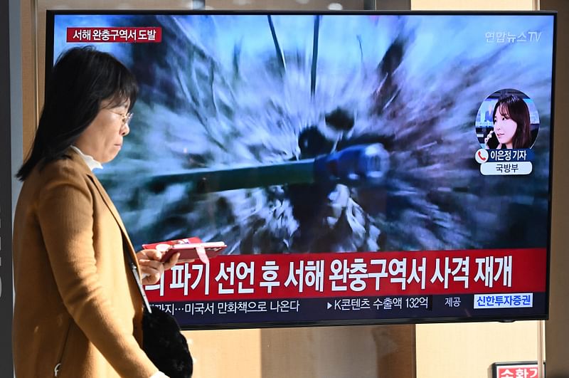 A woman walks past a television screen showing a news broadcast with file footage of North Korea's artillery firing, at a railway station in Seoul on 5 January 2024.