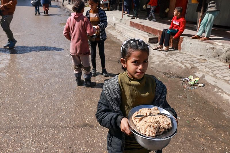 A displaced Palestinian child carries a plate of rice near a food distribution point in Rafah in the southern Gaza Strip on 8 March, 2024