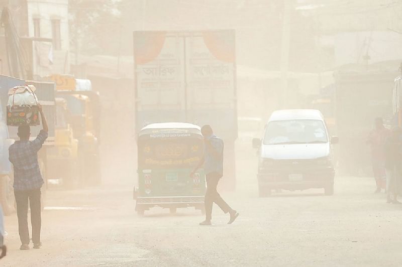 People cross the street as dust covers the Strand Road in the Sadarghat area of Chattogram city.