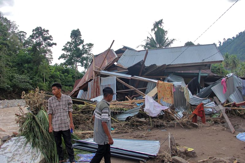 Villagers stand near a damaged house by a river after a flash flood at Pesisir Selatan in West Sumatra on 10 March 2024. The death toll from flash flooding and landslides on the Indonesian island of Sumatra has risen to 21, an official said on 10 March, with six people still missing.