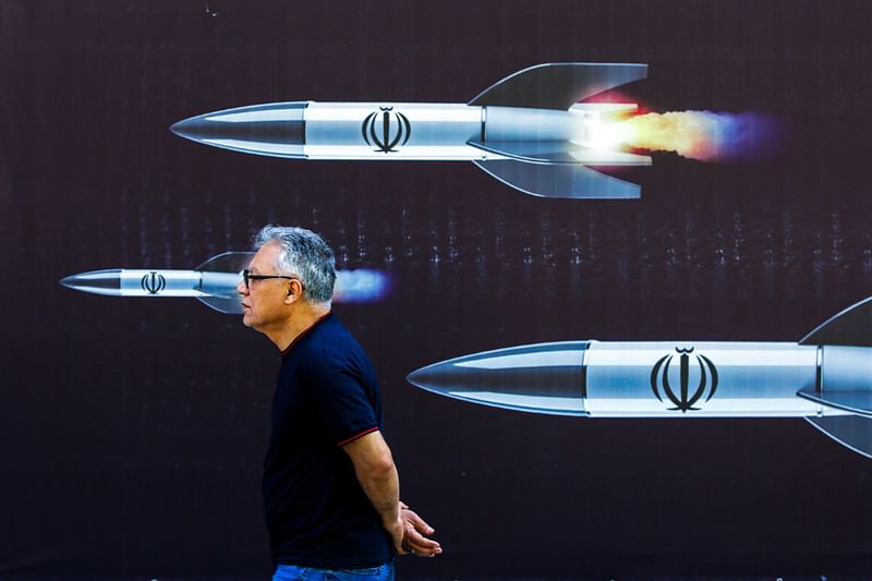 A man walks past a banner depicting missiles along a street in Tehran on 19 April, 2024. Iran's state media reported explosions in the central province of Isfahan on 19 April, as US media quoted officials saying Israel had carried out retaliatory strikes on its arch-rival